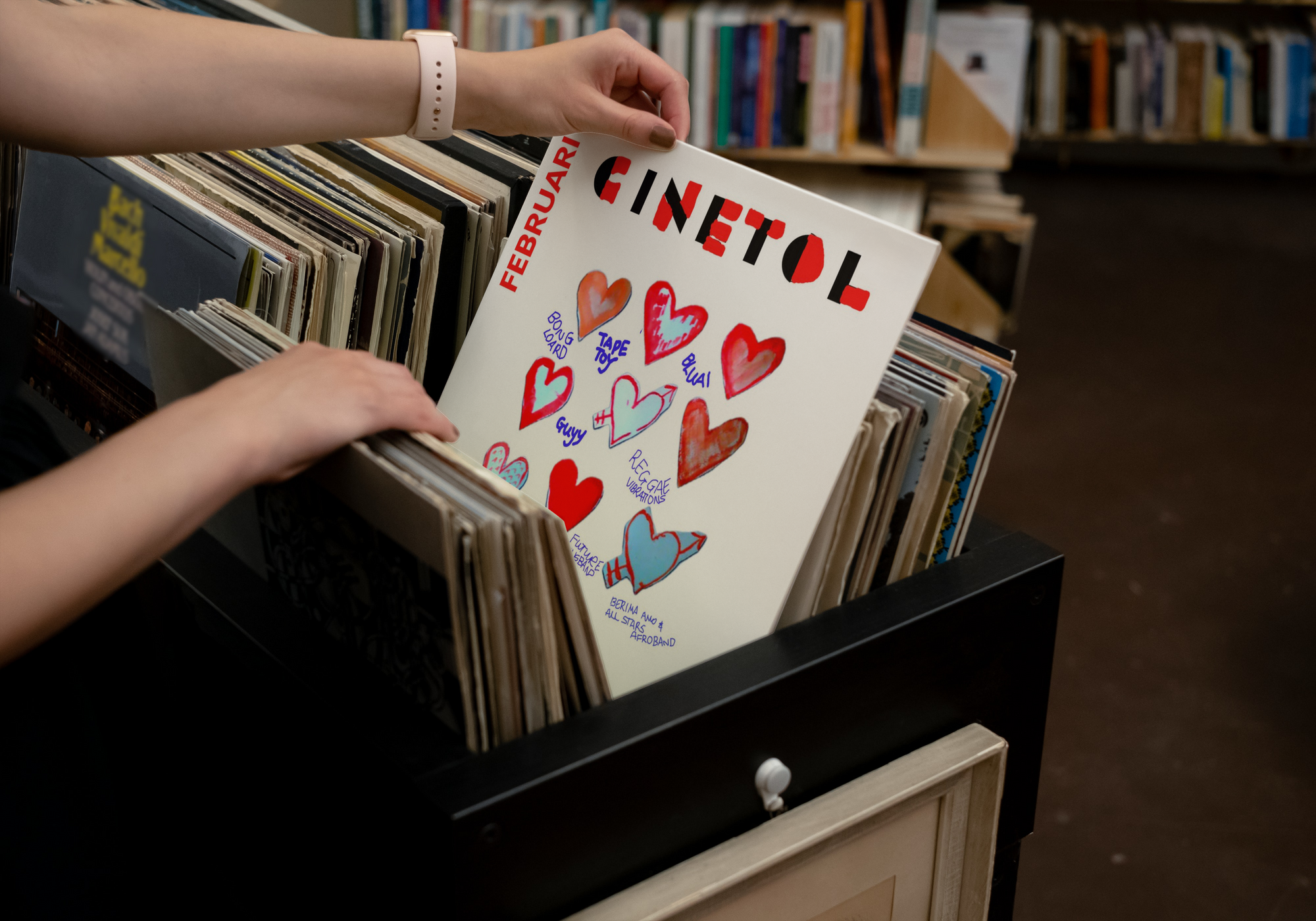 a person holding a vinyl record in front of a bookshelf with cinetol and hearts on it